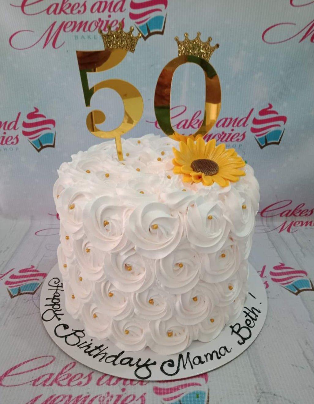 White 1-tier birthday cake with intricate icing rosettes, a large yellow sunflower, and gold 50th birthday toppers.