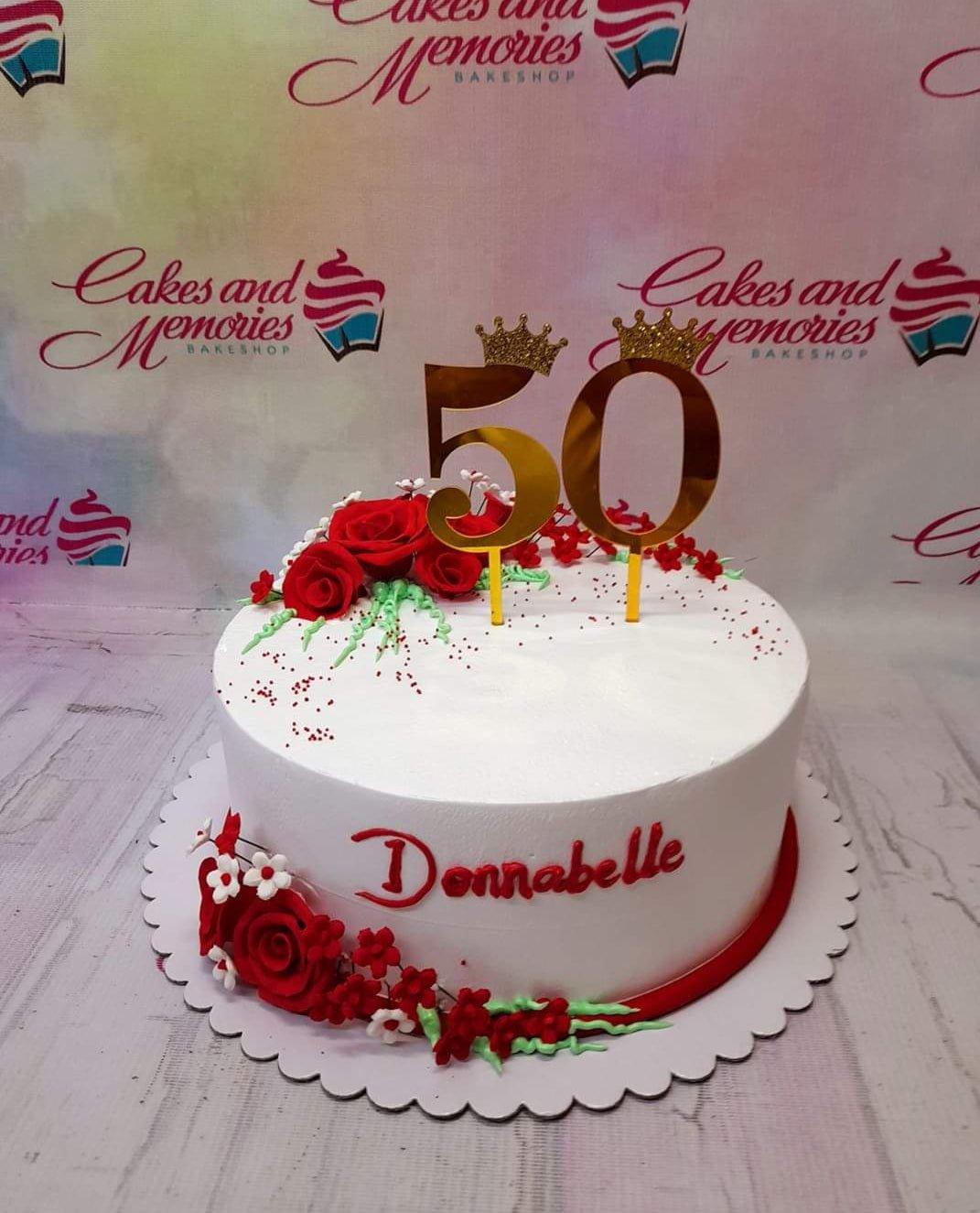 White 1-tier 50th birthday cake with red edible roses, gold number 50 topper with crowns, and red icing message Donnabelle.