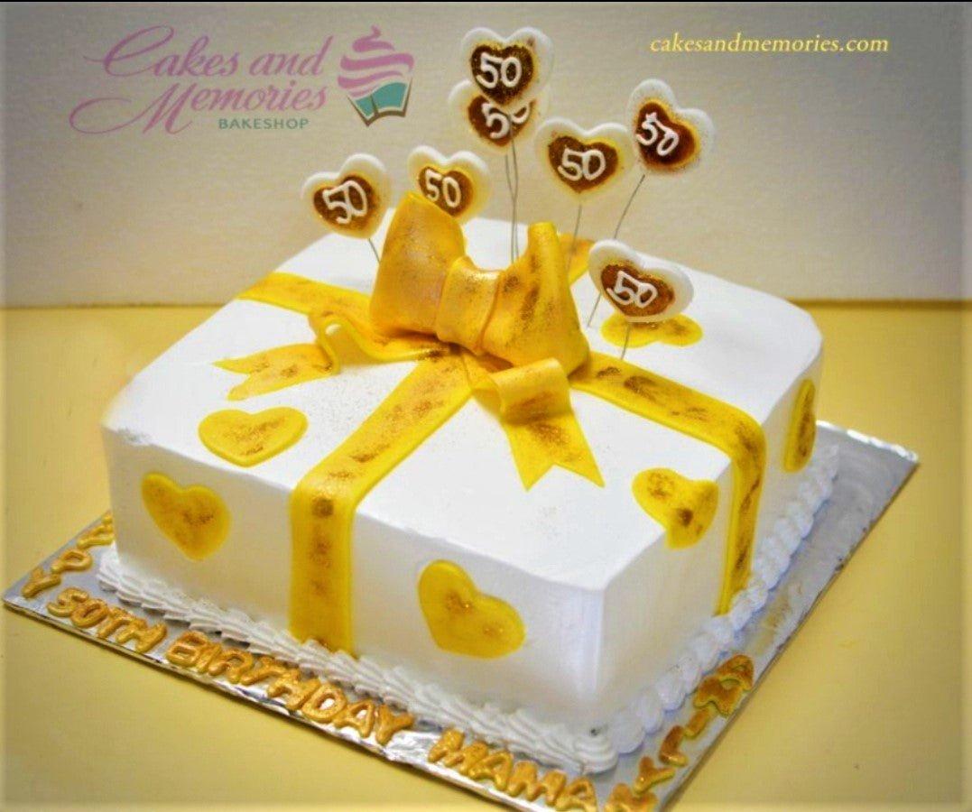 White square 50th birthday cake with yellow fondant ribbon bow and heart toppers featuring the number 50.