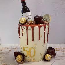 Tall white 1-tier cake with red wine bottle topper, chocolate truffles, grapes, and gold 50th birthday number.