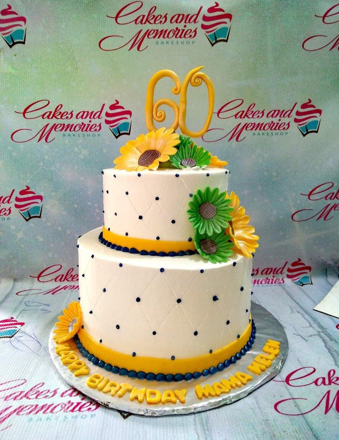 Two-tier white cake with yellow and green sunflowers, blue dots, and a gold number 60 topper.