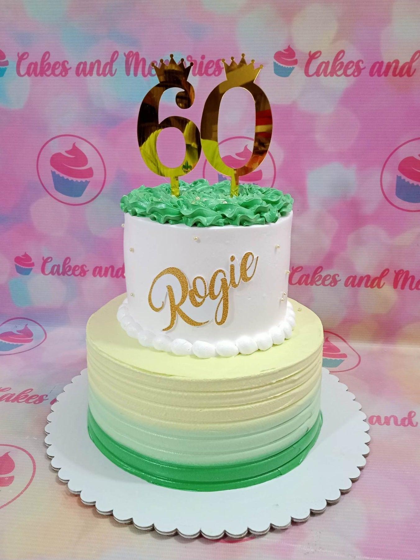 Two-tier green and white ombre cake with gold 60th birthday crown toppers and name Rogie in gold script.