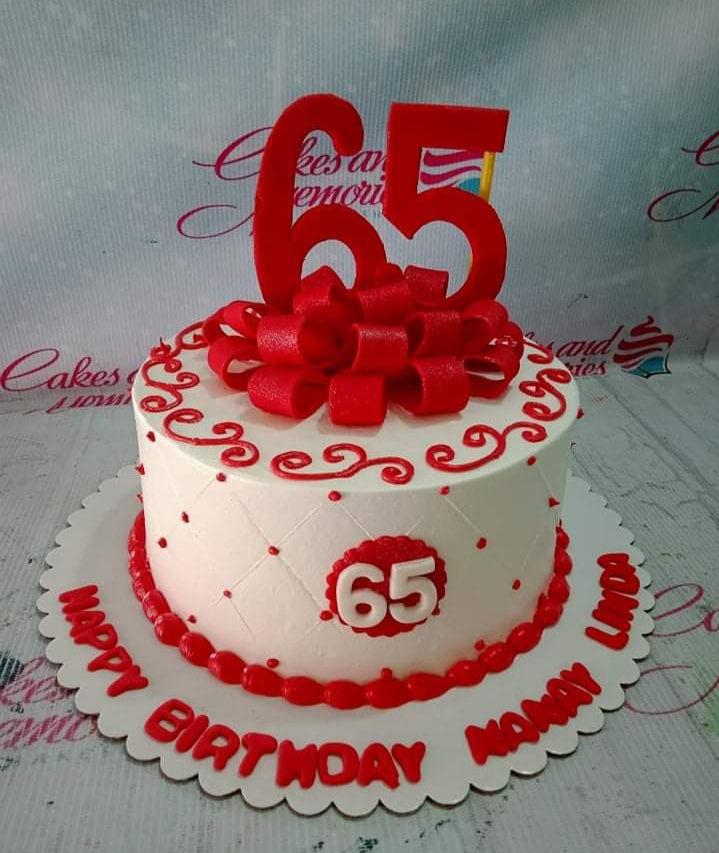 White 1-tier 65th birthday cake with red icing swirls, a large red fondant bow, and red number 65 toppers.