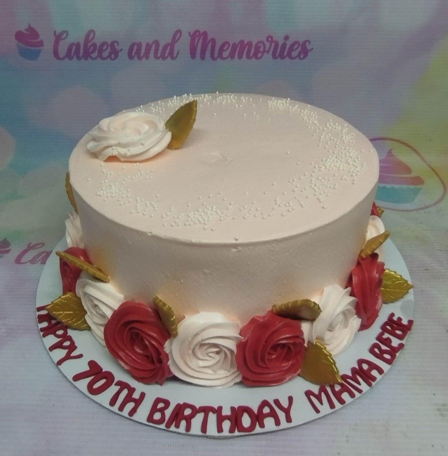 Elegant peach-colored 70th birthday cake with red and white icing roses and gold leaves around the base.