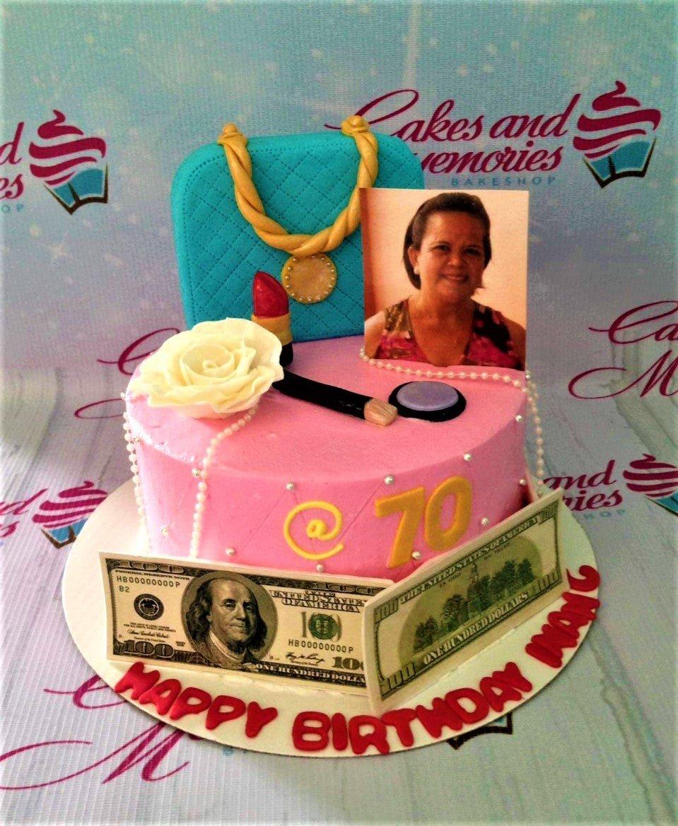Pink 70th birthday cake with a blue fondant bag, lipstick, makeup, photo topper, and edible hundred dollar bills.