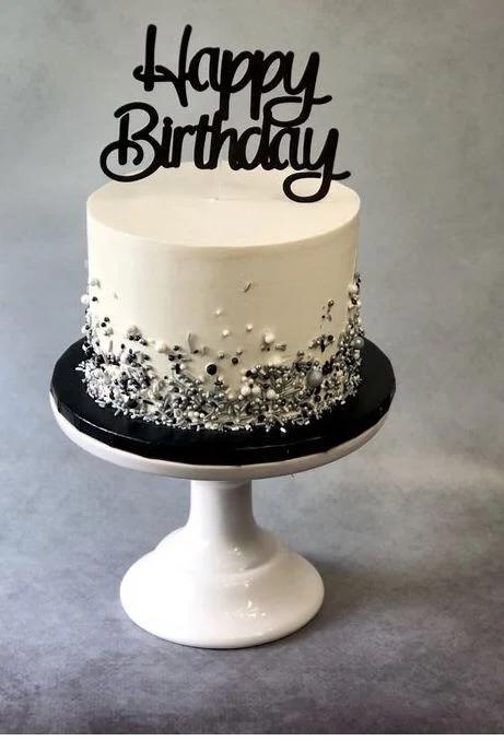 Elegant white minimalist birthday cake with black Happy Birthday topper and silver and black sprinkle base.