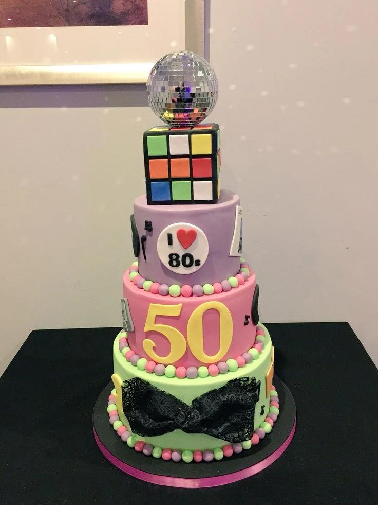 3-tier 80s themed birthday cake with Rubik's cube, disco ball, and neon colors for a 50th birthday celebration.