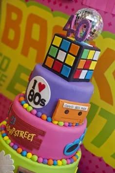 Vibrant 3-tier 80s themed fondant cake featuring a Rubik's cube, disco ball, cassette tape, and neon decorations.