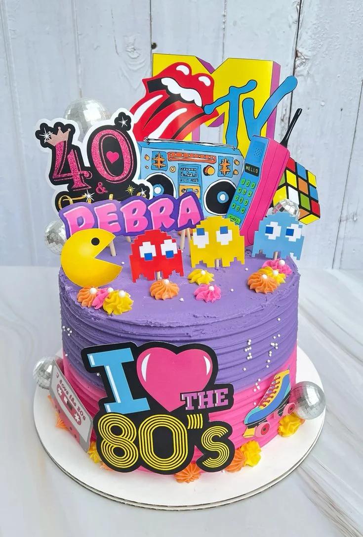 Vibrant purple and pink 80s themed birthday cake for Debra's 40th with Pac-Man, MTV, and Rubik's Cube toppers.