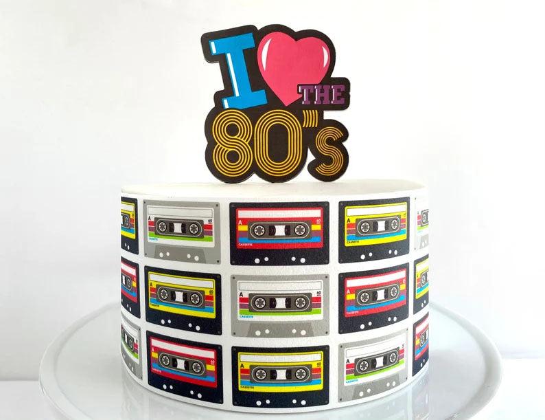 White 1-tier 80s themed cake featuring a large 'I Love the 80s' topper and a side wrap of colorful cassette tapes.