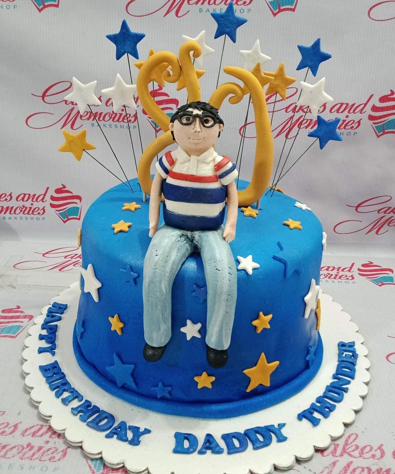 Blue fondant cake for an 80th birthday featuring a 3D fondant man figure, gold number 80, and blue, white, and gold stars.