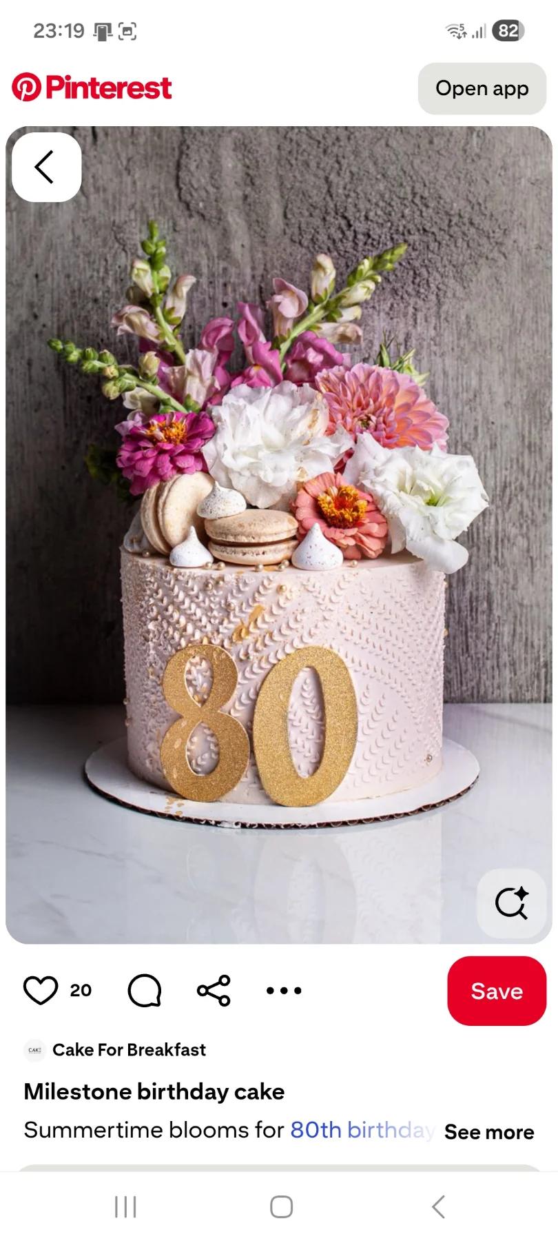 Elegant 80th birthday cake with a textured light pink icing, topped with fresh pink and white flowers, macarons, and a gold glitter number 80.