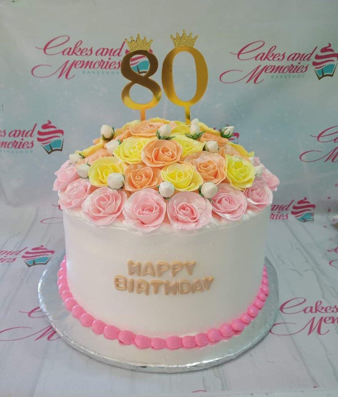 White 1-tier 80th birthday cake topped with a dome of pink, yellow, and peach icing roses and gold number 80 toppers.
