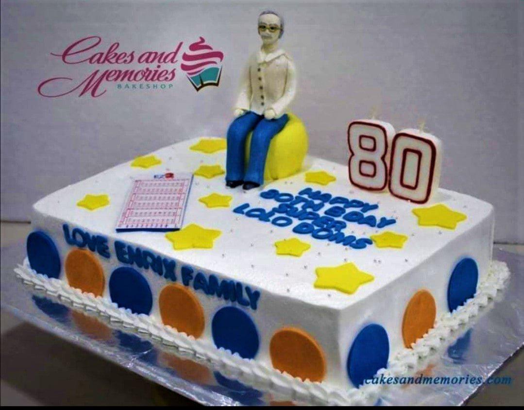 White rectangular 80th birthday cake with a fondant man figure sitting on a yellow ball, yellow stars, and blue and orange side circles.