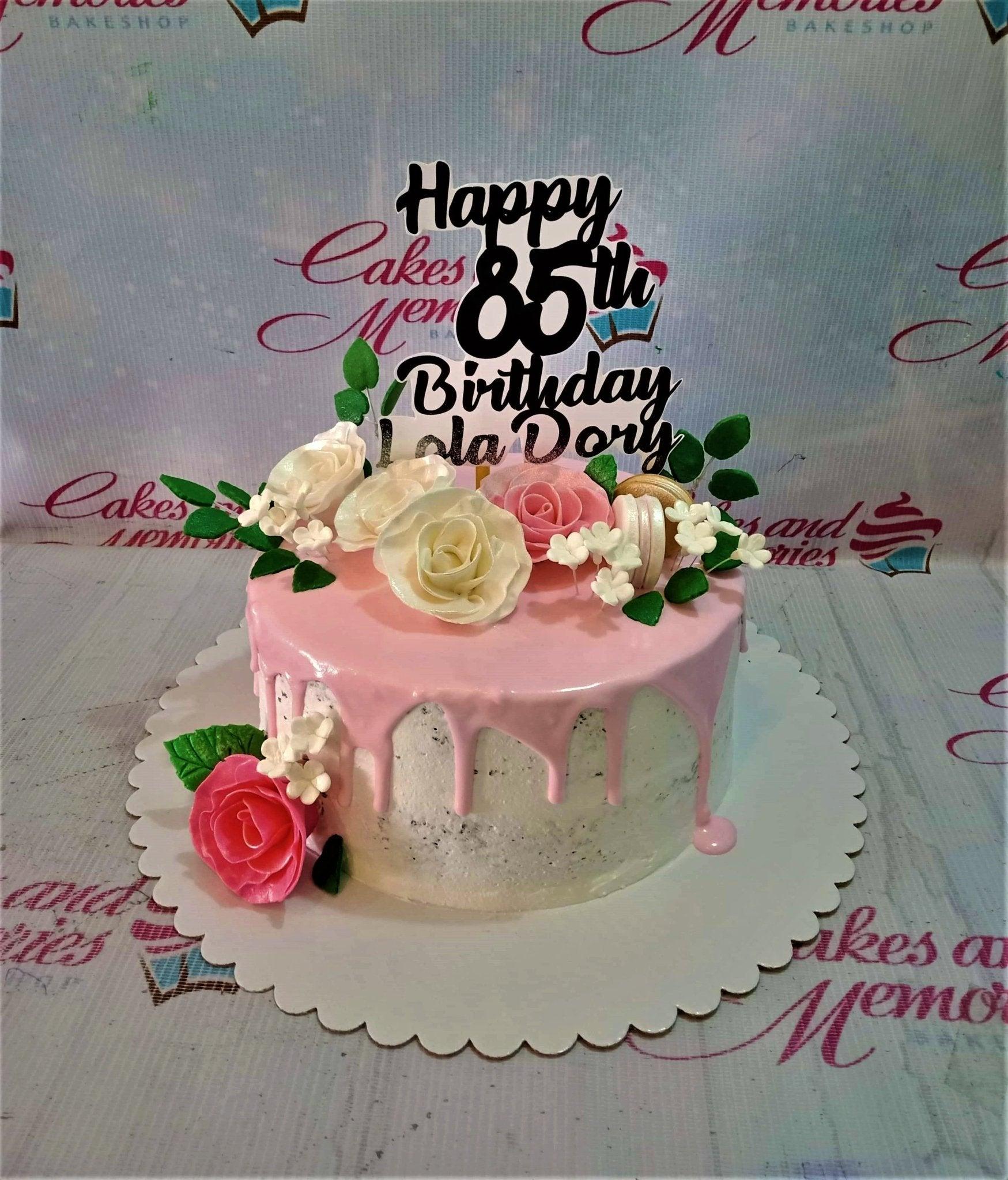 Pink and white 85th birthday cake for Lola Dory with pink icing drip, edible roses, and a black custom topper.