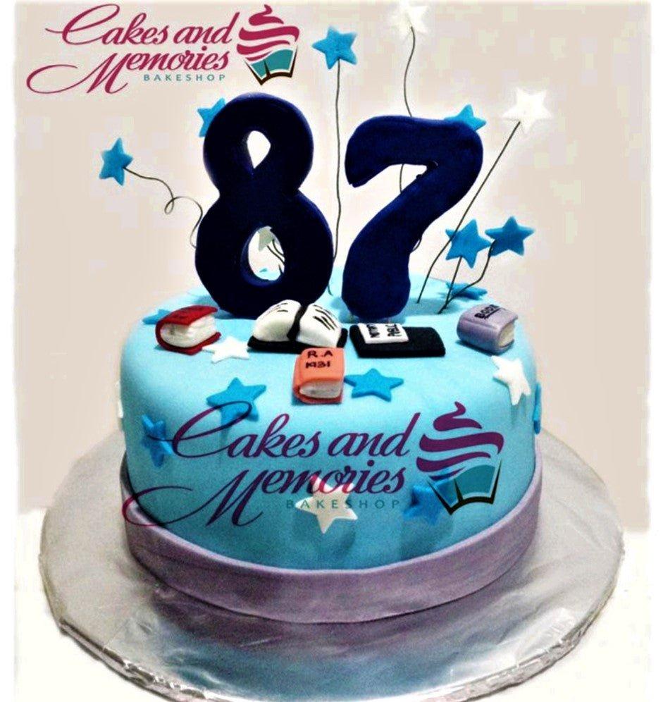 Light blue fondant cake for an 87th birthday featuring large navy blue number toppers, fondant books, and blue and white stars.