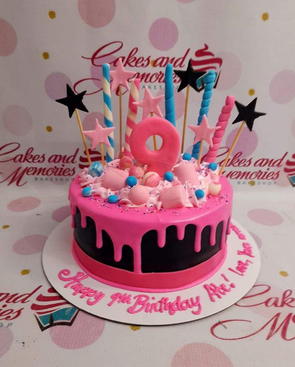 Pink and black 9th birthday cake with pink drip, marshmallows, and colorful star and spiral toppers.