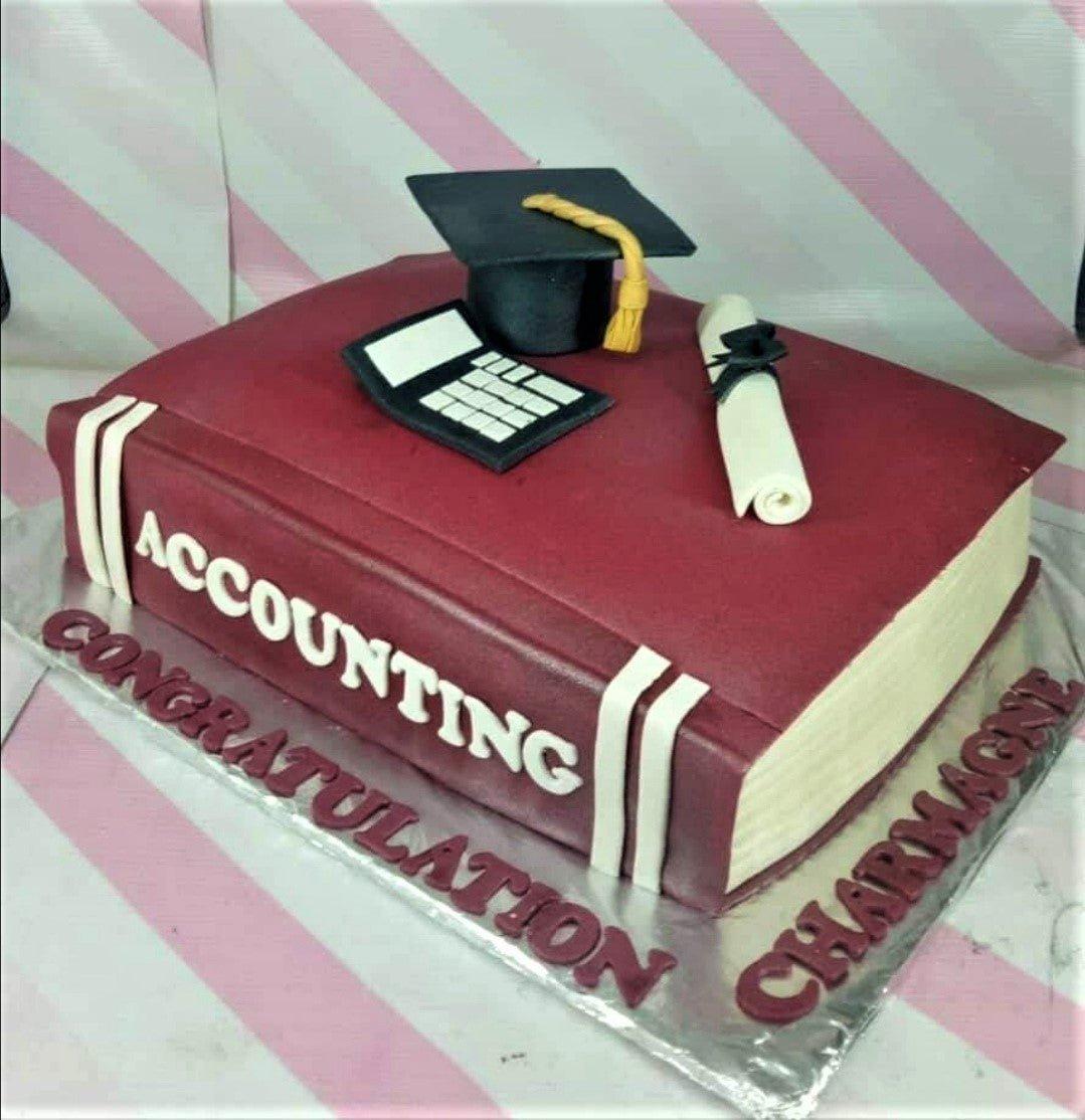 Maroon book-shaped accounting graduation cake with a black graduation cap, diploma, and calculator toppers.
