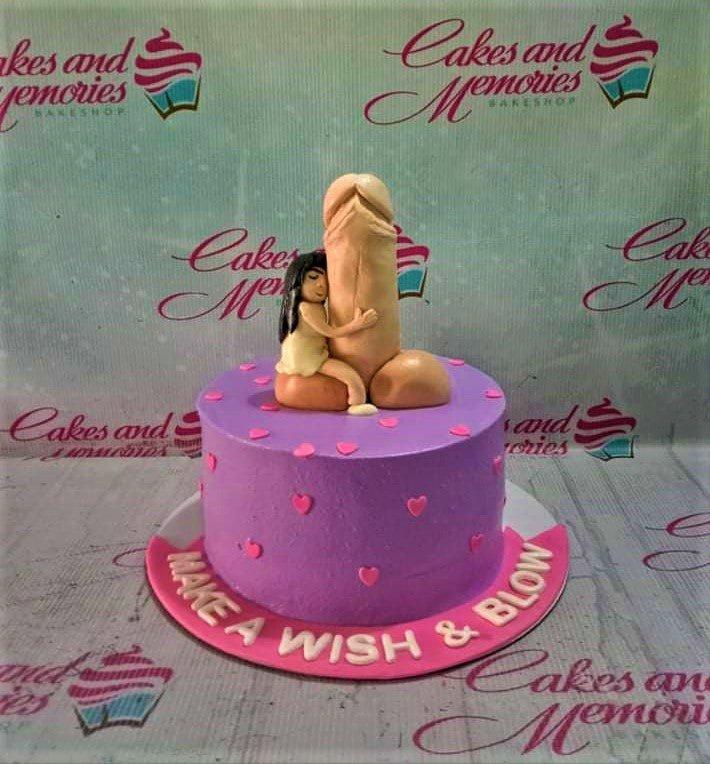 Purple adult-themed birthday cake with a humorous 3D fondant topper of a woman hugging a large phallic symbol and pink heart decorations.