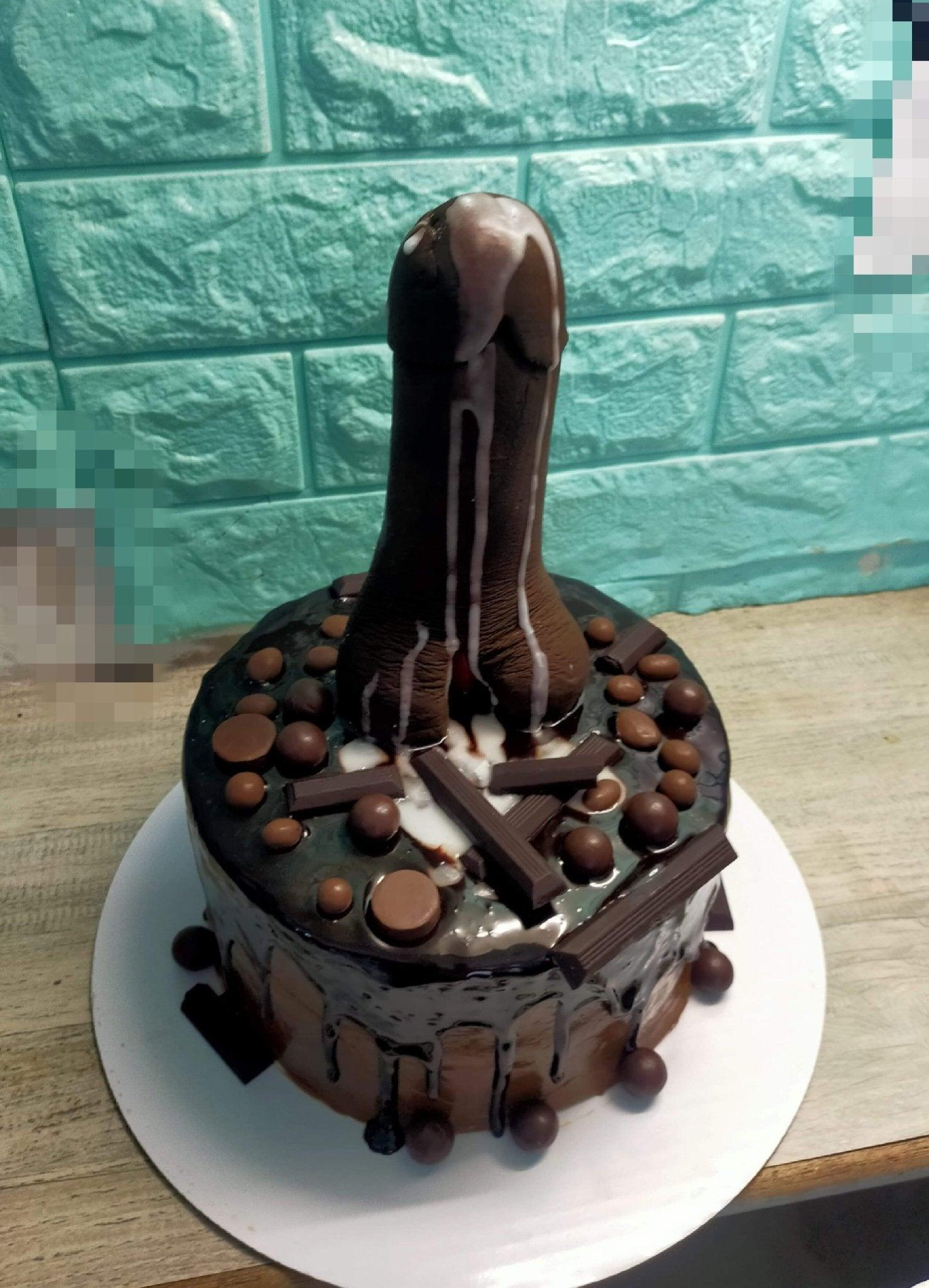 Chocolate drip cake with a large brown phallic-shaped fondant topper and chocolate bar decorations.