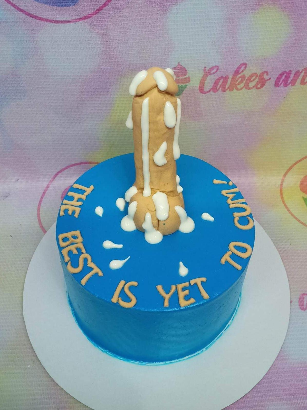 Blue minimalist cake with a tan 3D phallic topper and white icing drips, featuring the message 'THE BEST IS YET TO CUM!'