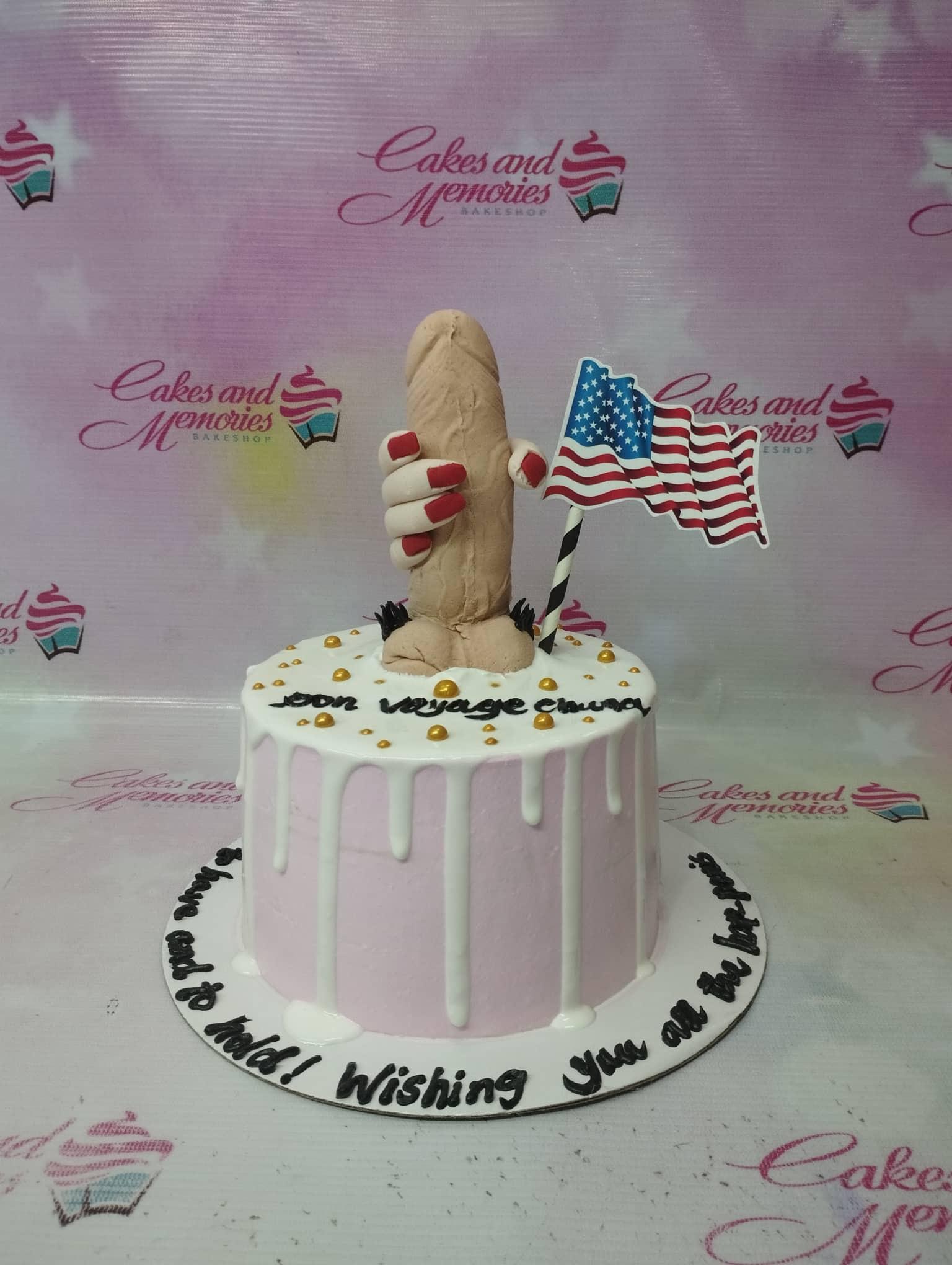 Pink drip cake with a humorous 3D fondant figure holding an American flag printout and gold sprinkles.