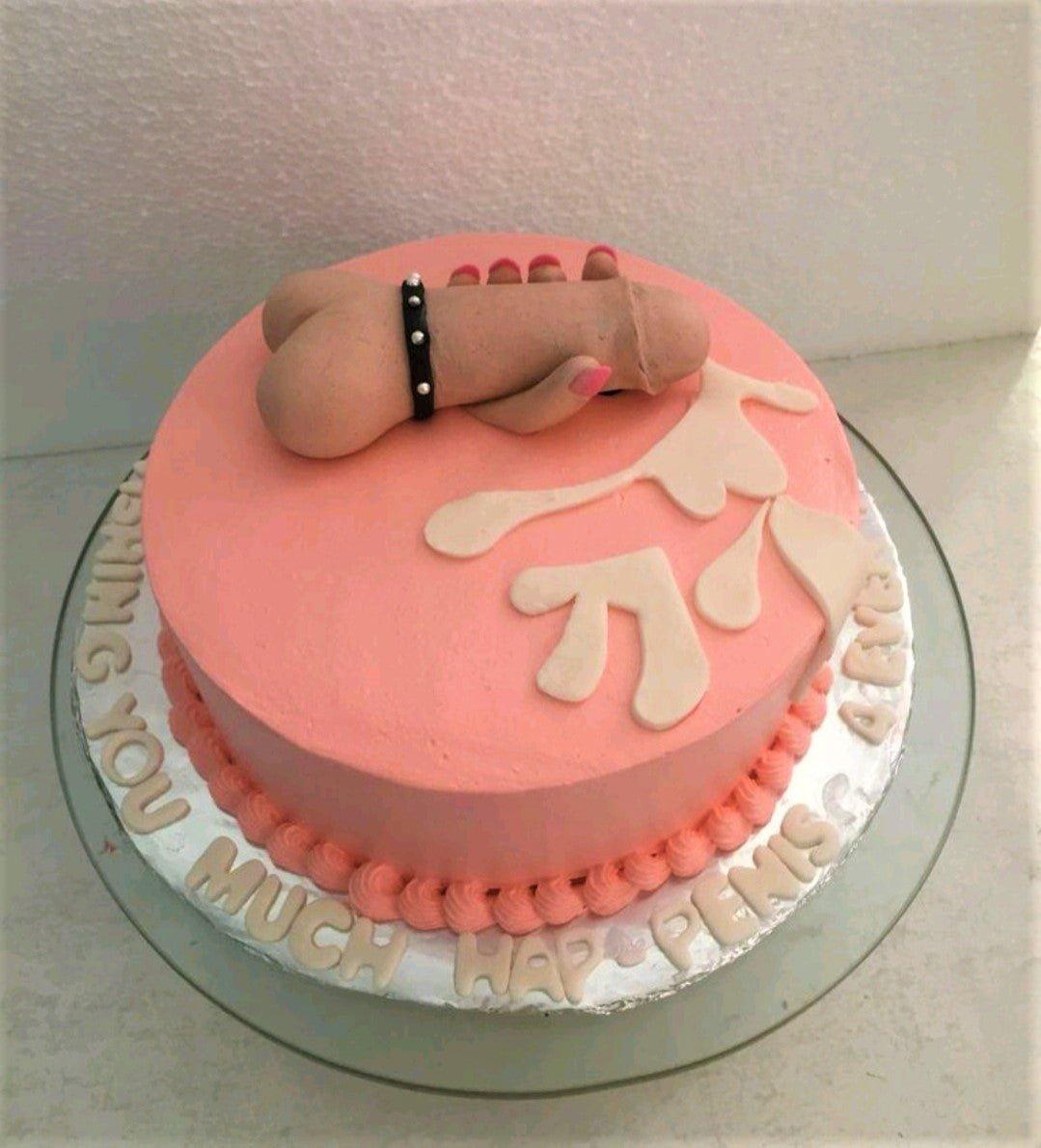 Pink round cake with a humorous adult theme featuring a 3D fondant phallic topper and cream-colored icing splatters.
