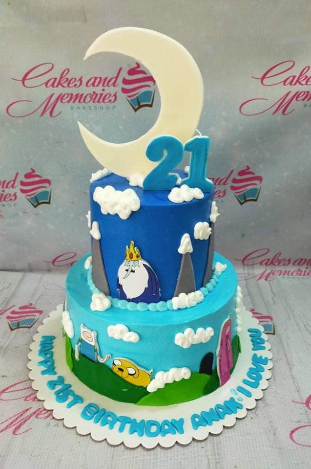 Two-tier Adventure Time themed cake with blue icing, fondant clouds, mountains, and character printouts of Finn, Jake, Ice King, and Princess Bubblegum.