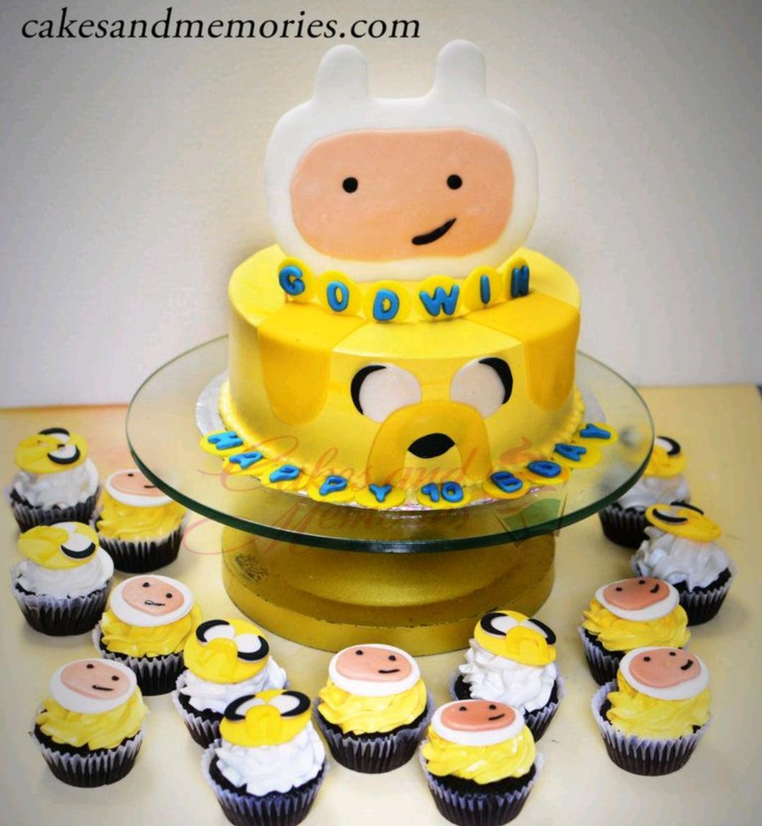 Yellow Adventure Time themed cake featuring Jake the Dog's face on the side and a large Finn the Human fondant topper on top.