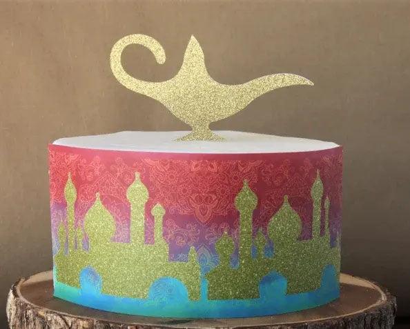 Aladdin themed cake with a gold glitter magic lamp topper and a colorful silhouette of an Arabian palace on the side.