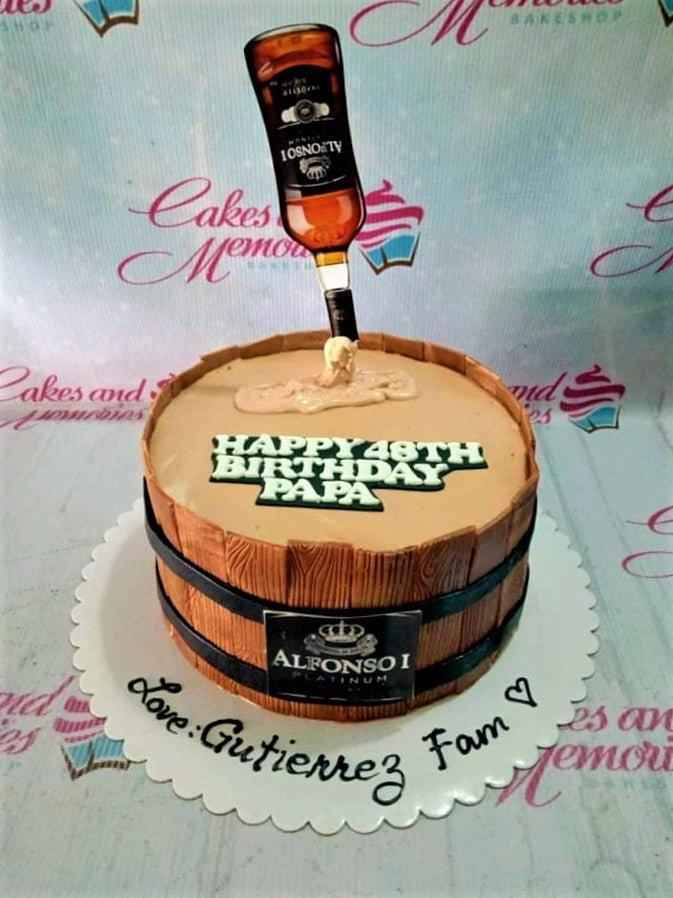 A barrel-shaped cake designed to look like a wooden whiskey barrel with an Alfonso I Platinum bottle topper pouring liquid.