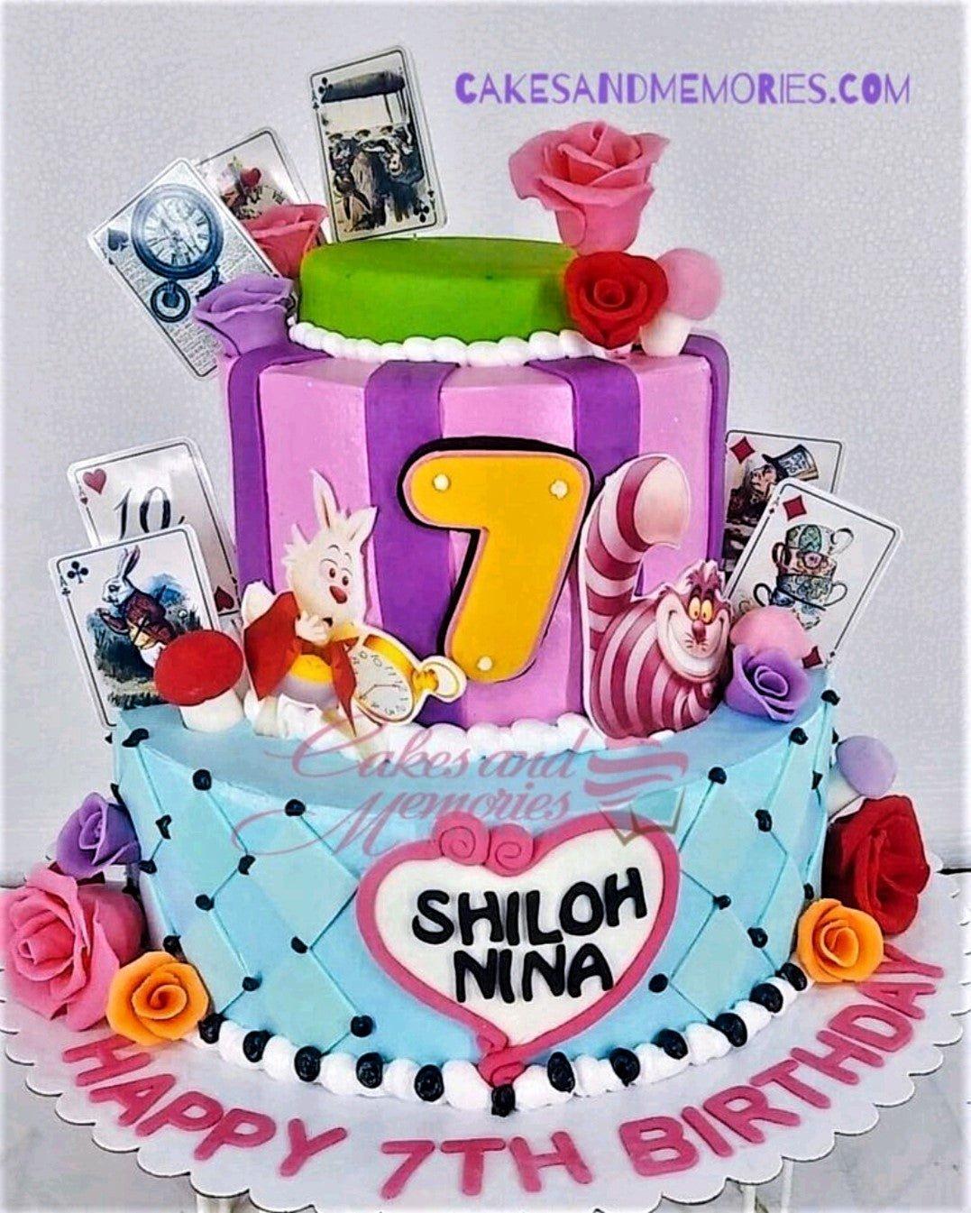 Alice in Wonderland themed 2-tier cake with White Rabbit, Cheshire Cat, playing cards, and roses in pink, purple, and blue.
