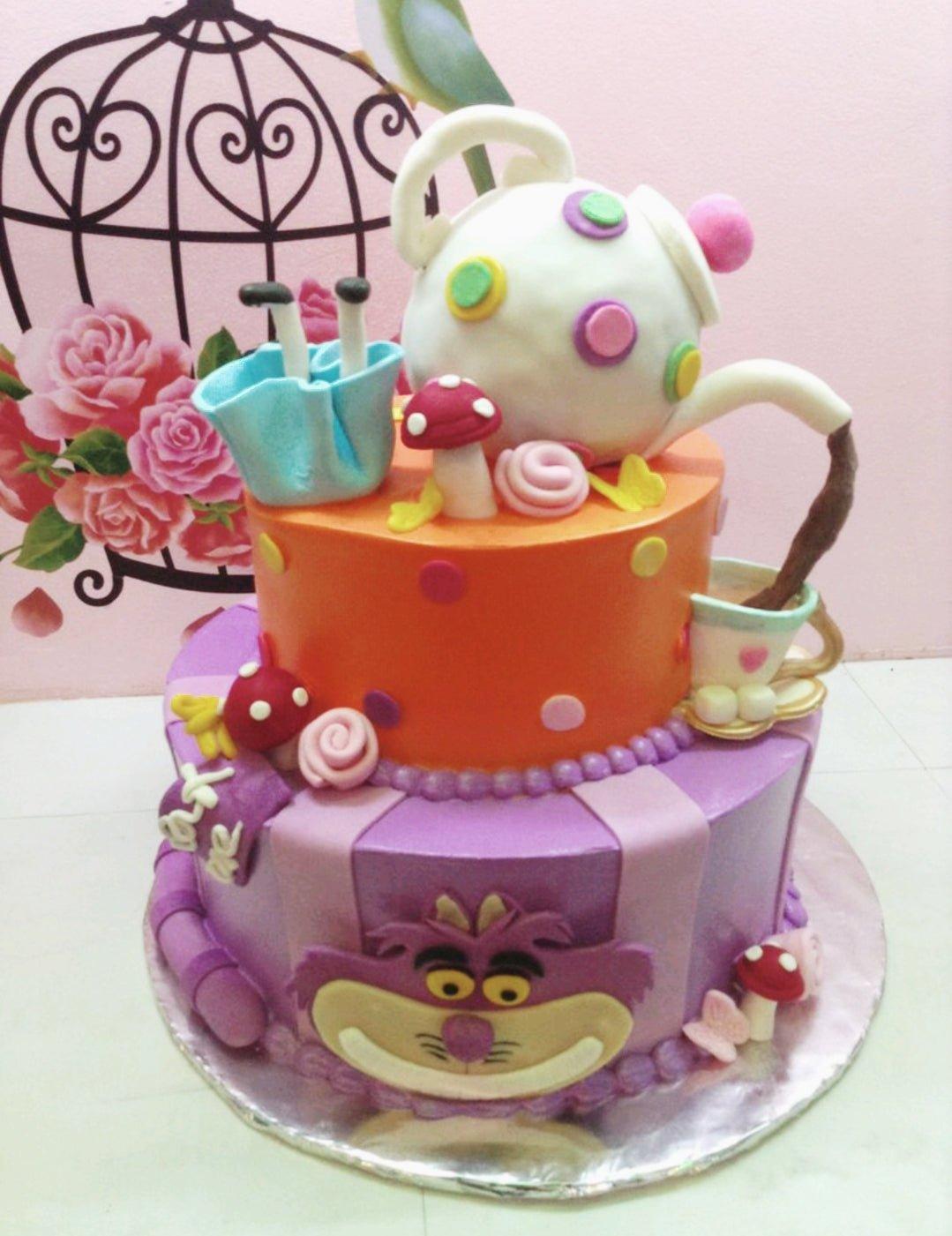 Alice in Wonderland themed 2-tier fondant cake with a teapot topper, Cheshire Cat face, and whimsical mushrooms.