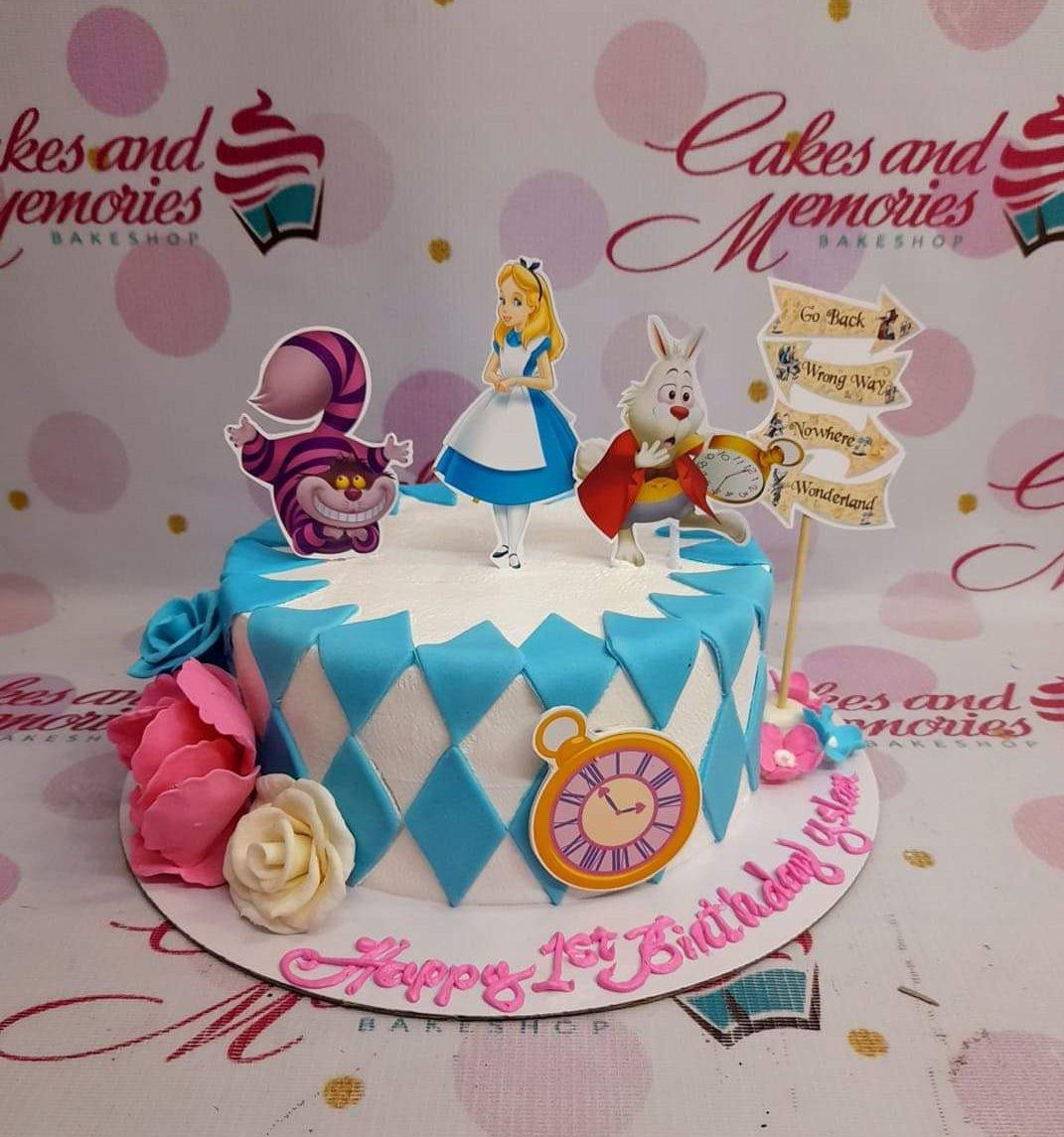 Alice in Wonderland themed birthday cake with blue and white diamond pattern, fondant roses, and character printouts.