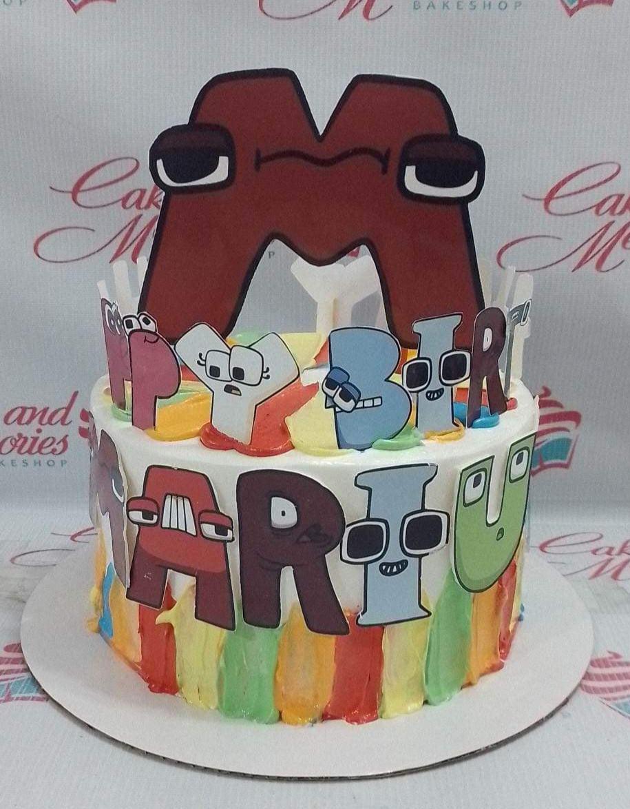 Alphabet Lore themed birthday cake with colorful icing stripes and character printouts including a large letter M topper.