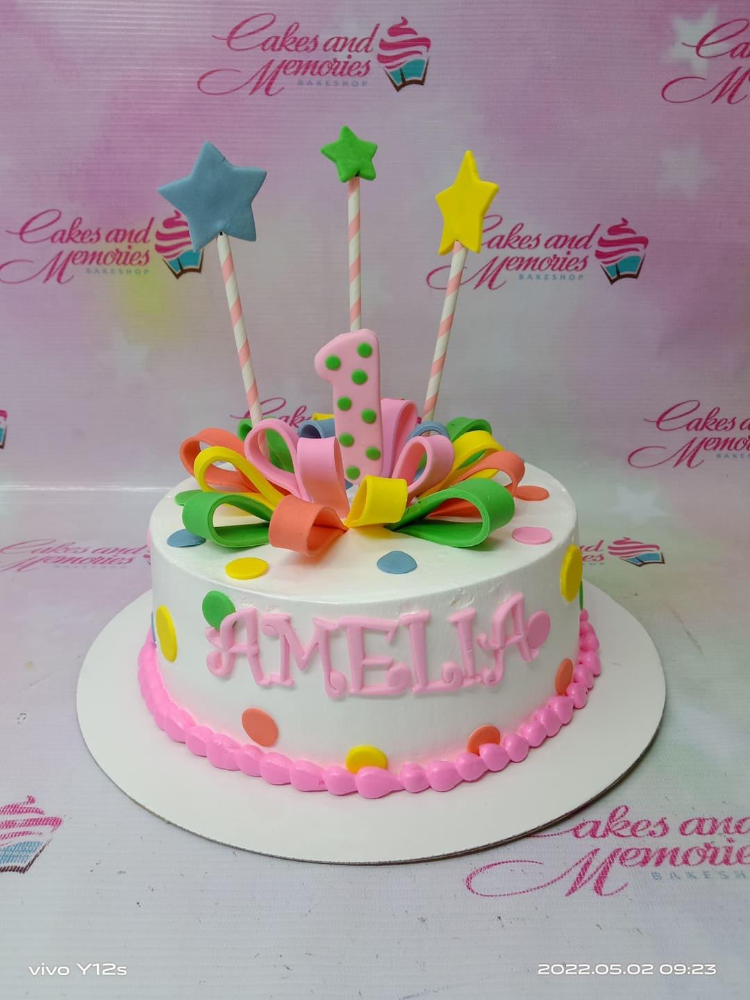 White 1-tier birthday cake for Amelia with colorful fondant loops, a pink number one topper, and star toppers on sticks.