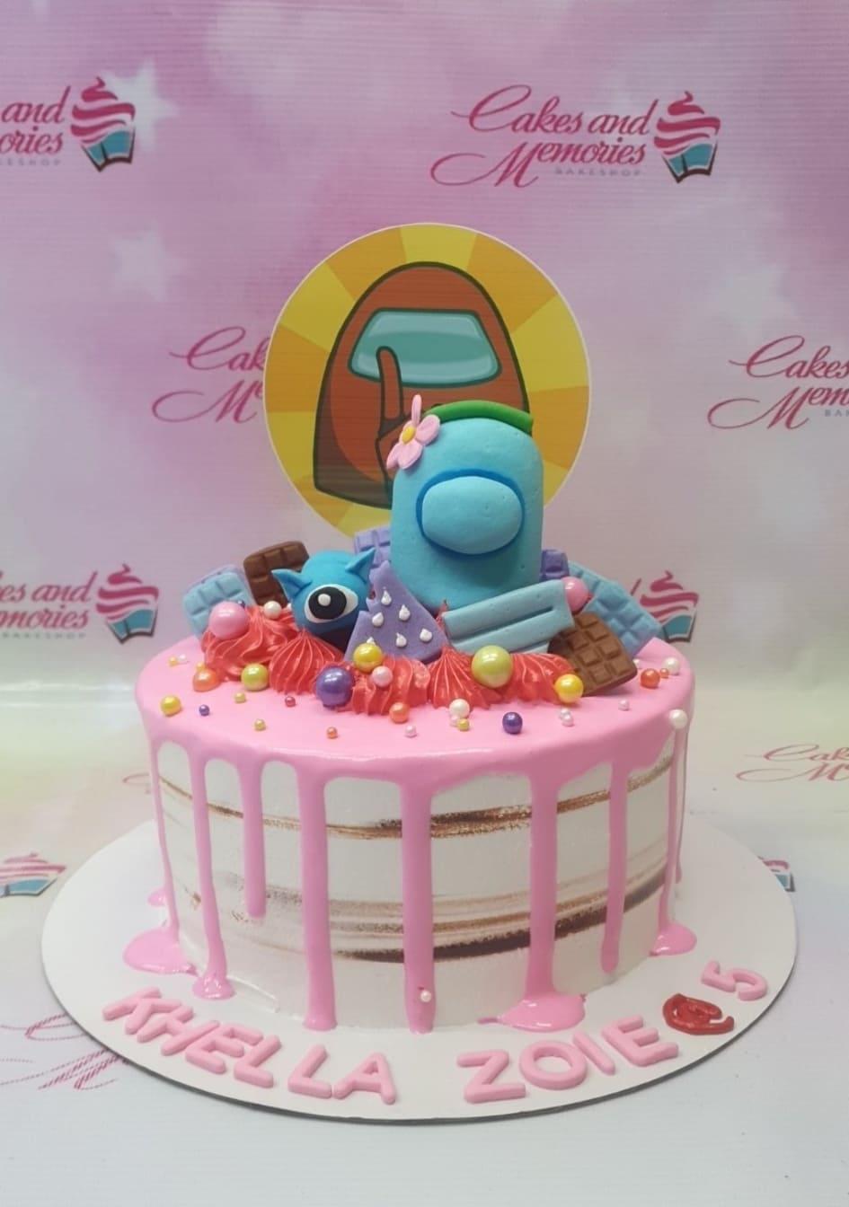 Pink Among Us themed cake with a blue character topper, chocolate bars, and colorful sprinkles on a semi-naked icing base.