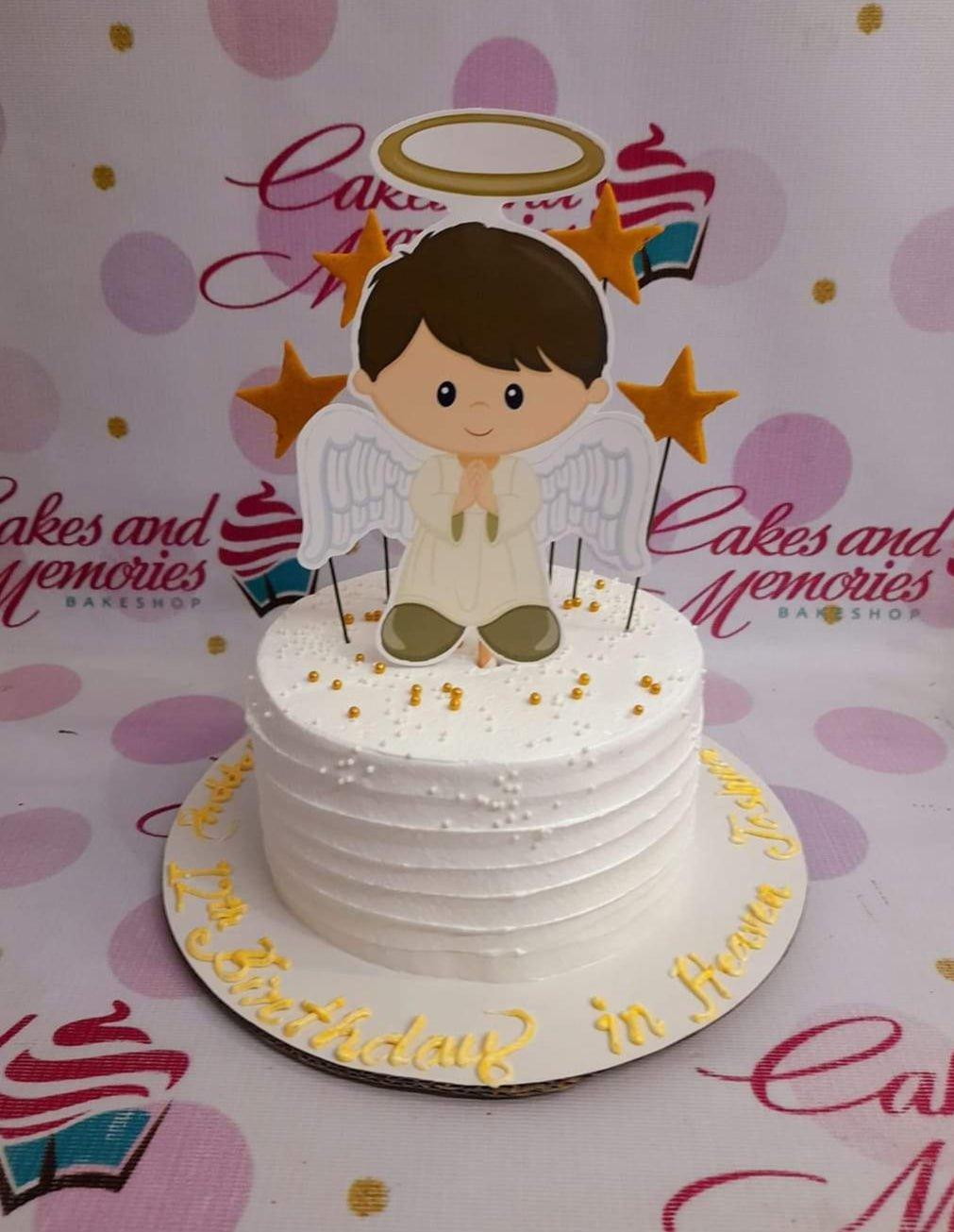 White 1-tier angel birthday cake with a boy angel printout topper, gold stars, and gold dragees on a white soft-icing base.