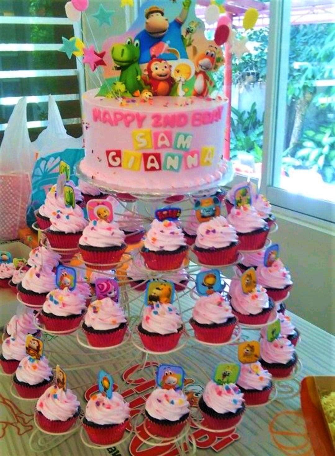Pink 1-tier birthday cake with animal character printouts and matching cupcakes on a tiered stand.