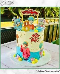 Blue and white anime themed birthday cake with character printouts, a soda pop topper, and yellow icing rosettes.