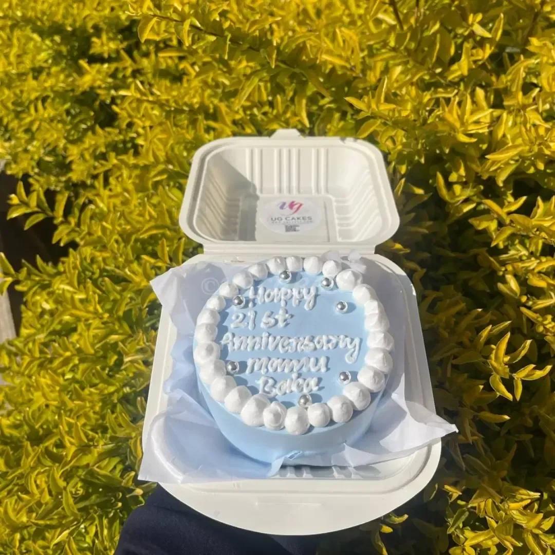 Light blue bento cake with white icing dollop border and silver dragees for a 21st anniversary celebration.