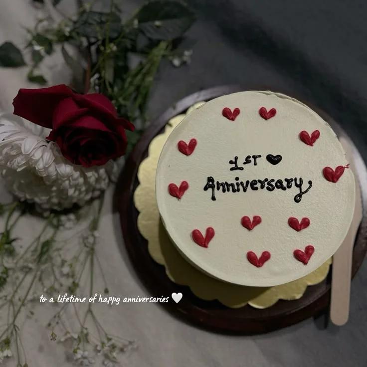 White bento cake with red icing hearts and black anniversary message on a gold board.
