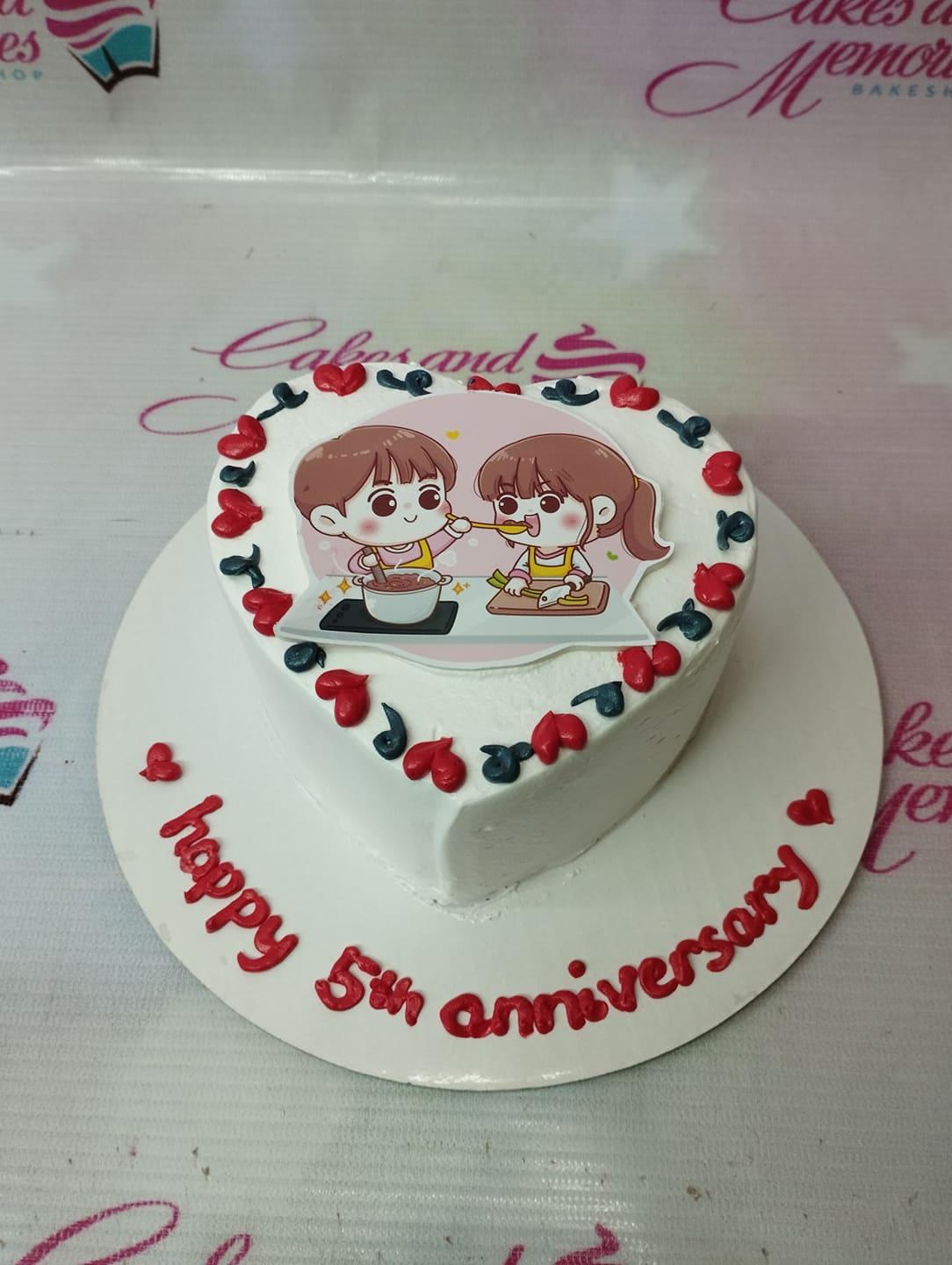 Heart-shaped white bento cake for a 5th anniversary featuring a cute couple printout and red and navy blue icing hearts.