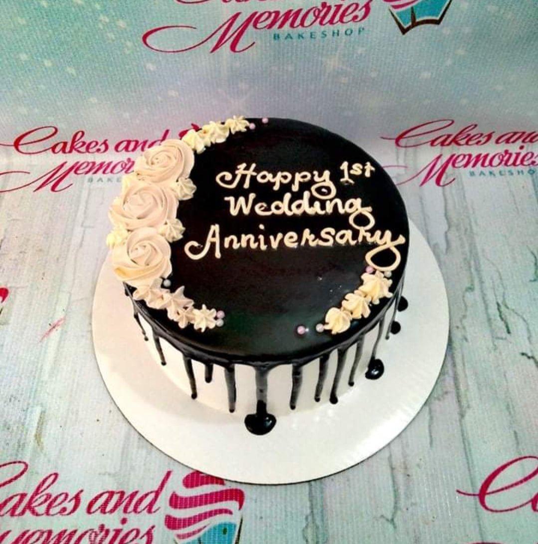Single tier white cake with dark chocolate drip, cream-colored icing roses, and a Happy 1st Wedding Anniversary message.