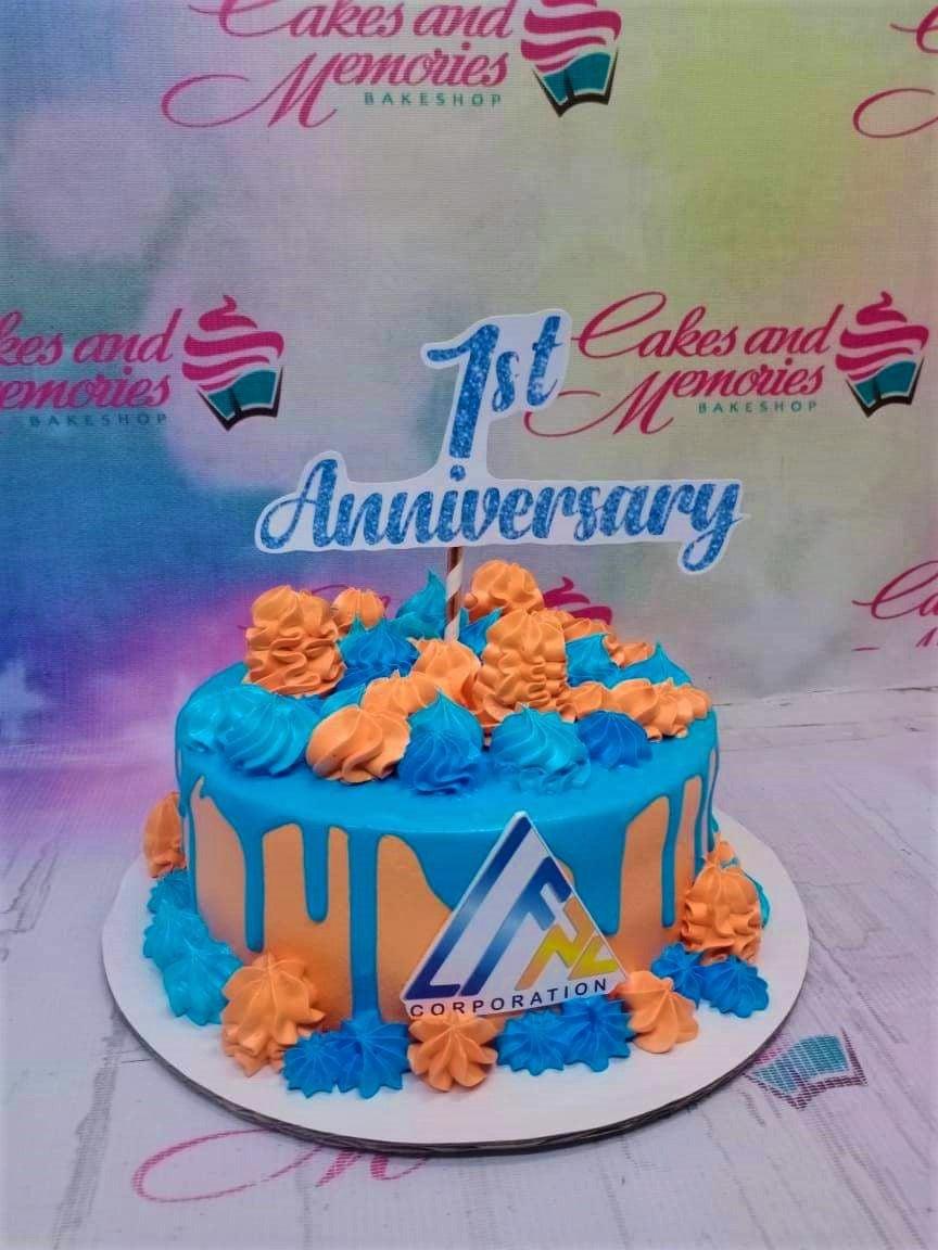 Blue and orange 1st anniversary cake with blue icing drip, piped rosettes, and a corporate logo topper.
