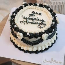 Elegant black and white vintage-style 2nd wedding anniversary cake with intricate piping and white roses.