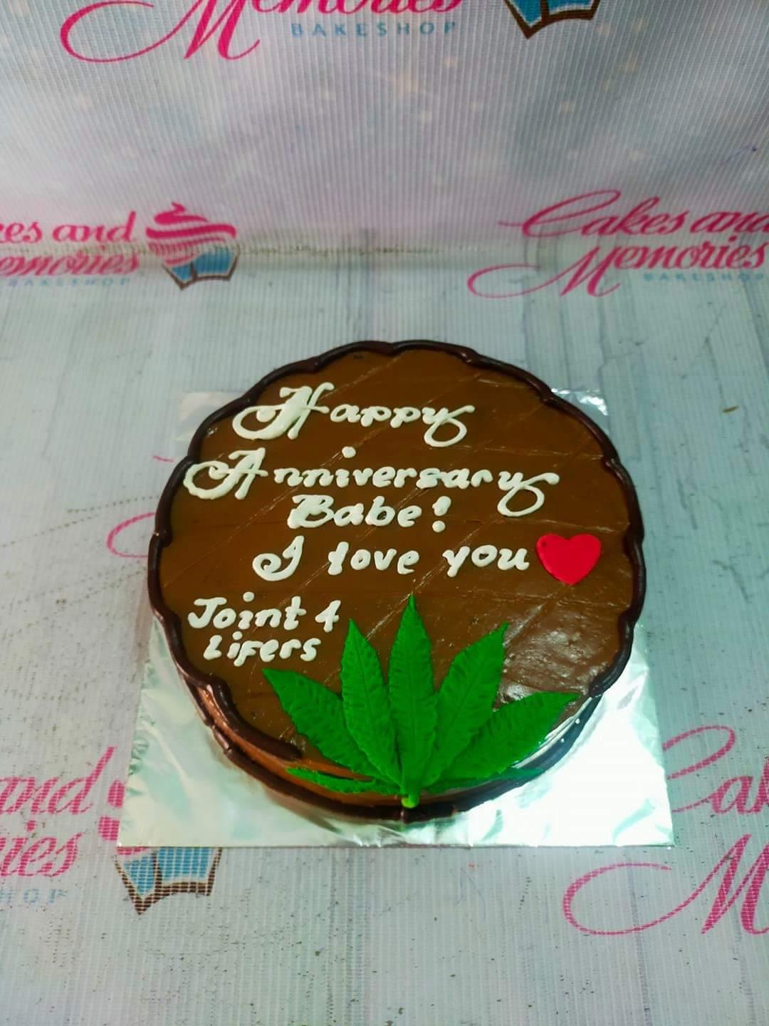 Chocolate brown round cake with white icing message and a green fondant leaf for an anniversary celebration.
