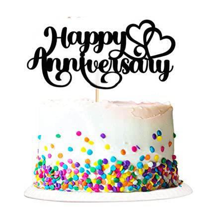 White soft-icing anniversary cake with colorful confetti sprinkles and a black Happy Anniversary topper with hearts.