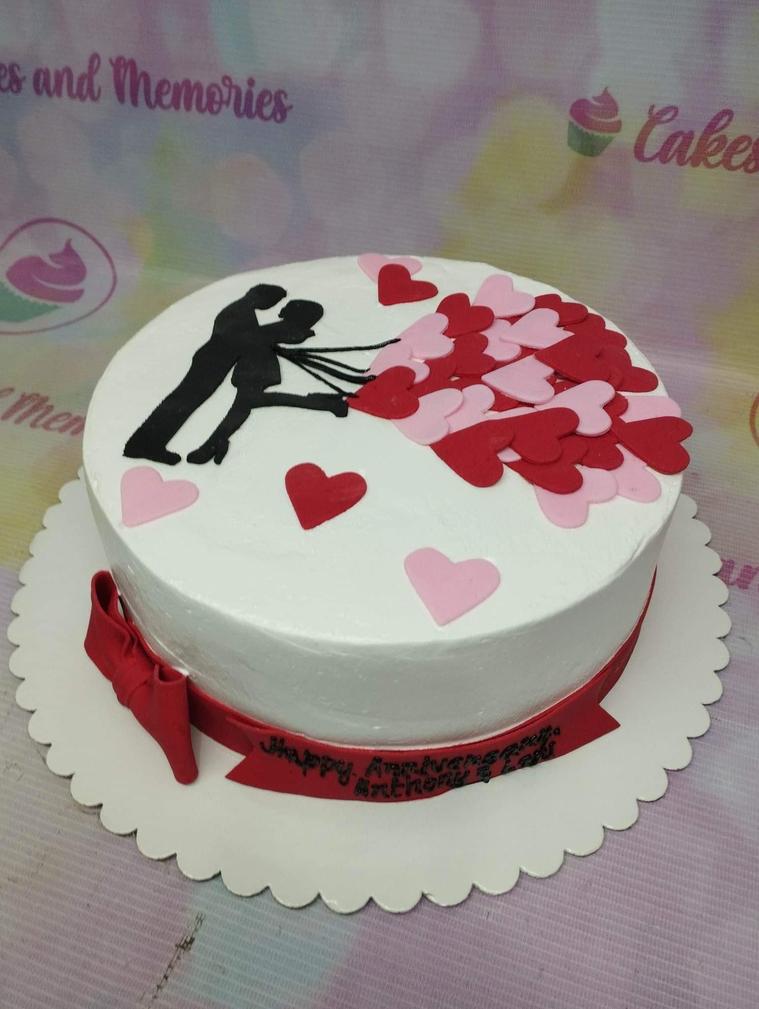 White round anniversary cake with a black silhouette of a couple holding heart-shaped balloons in pink and red.
