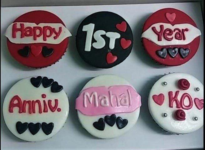 Six custom cupcakes with red, black, and white fondant tops featuring anniversary messages and heart decorations.